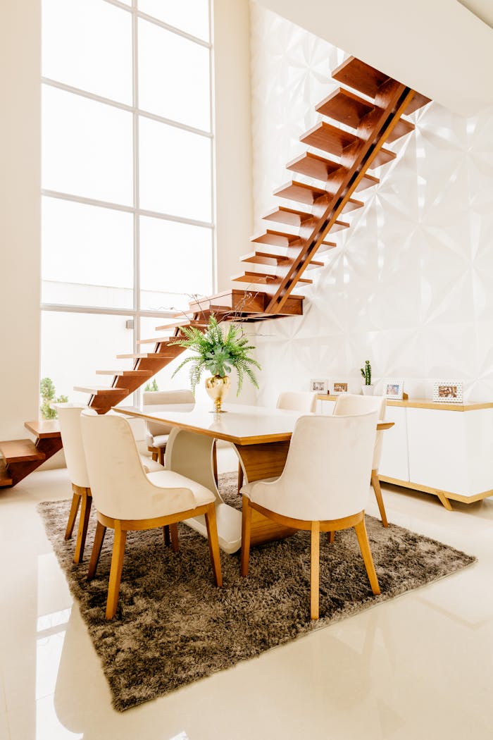 Minimalistic design of spacious room with second level space and wooden staircase against large windows in modern house in daytime